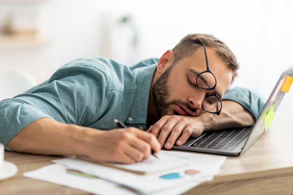 Exhausted,Millennial,Man,Sleeping,On,His,Office,Desk,,Next,To