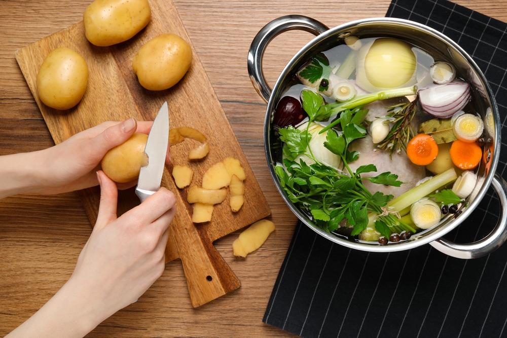 Frau,schält,Kartoffel,zum,Kochen,schmackhafte,Bouillon,am,hölzernen,Tisch,